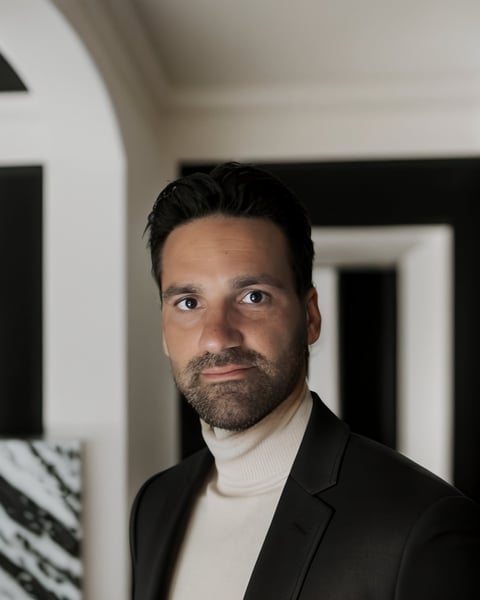 Nadim Jovicic, Hygieneplan-Experte, im Portrait mit dunklen Haaren und Bart, schwarzer Blazer mit cremefarbenem Rollkragenpullover